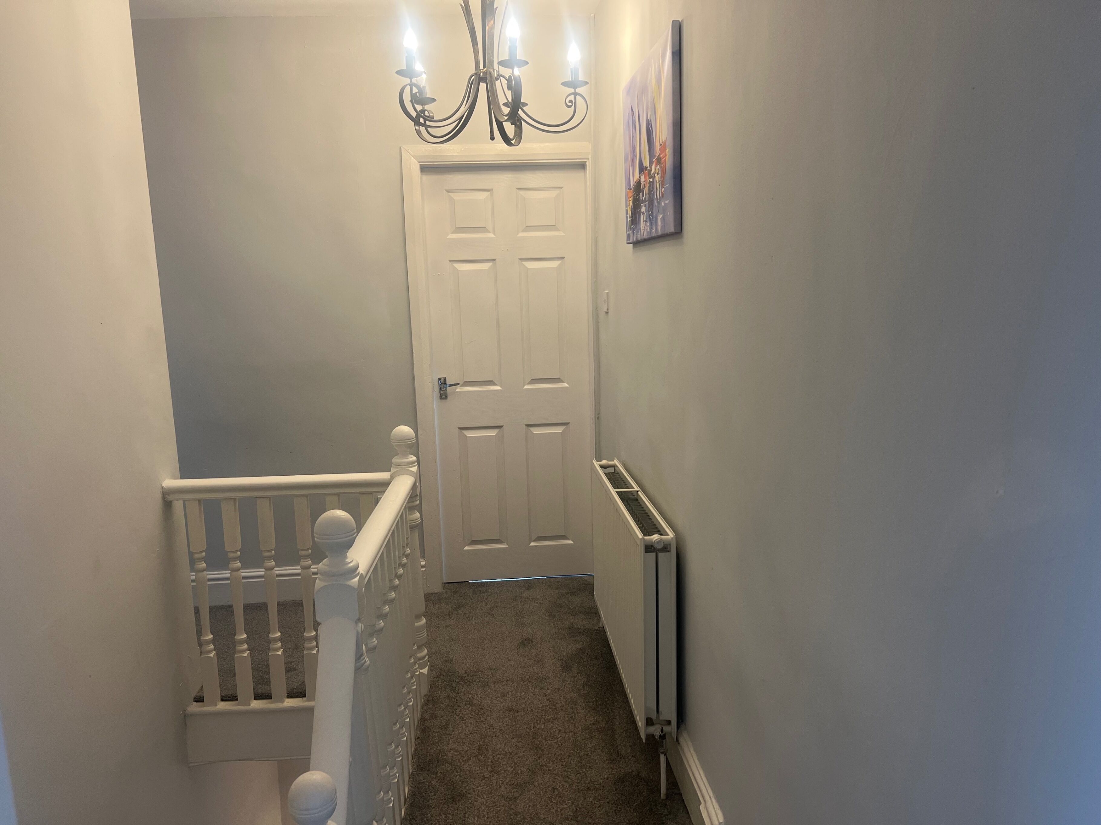 A hallway with a white door, a radiator, and a chandelier.