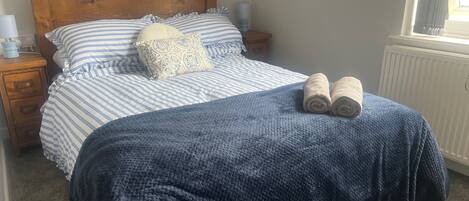 A neatly made bed with striped bedding, a blue blanket, and rolled towels.