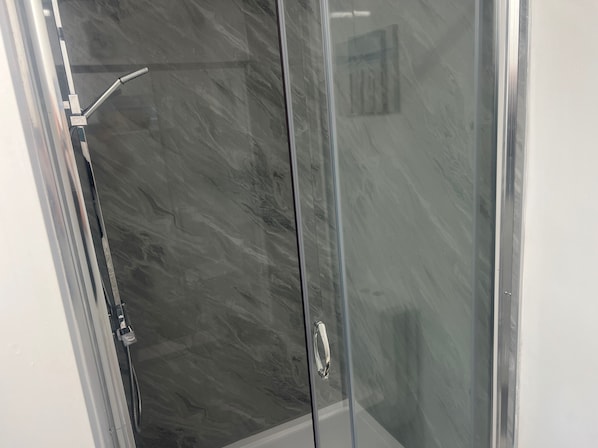 A glass-enclosed shower with a marble-like wall and a chrome handle.