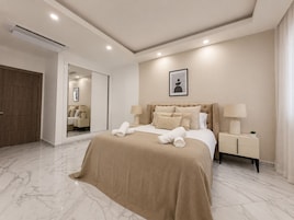 Un dormitorio de hotel moderno con una cama grande, mesitas de noche, un espejo y una lámpara en el techo.