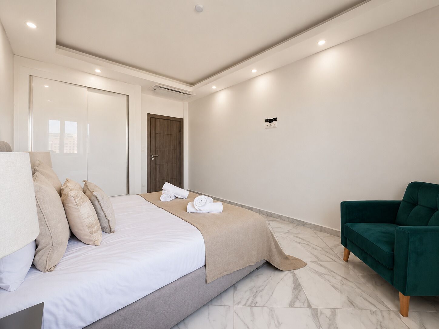 A modern bedroom with a bed, a green chair, and a door.