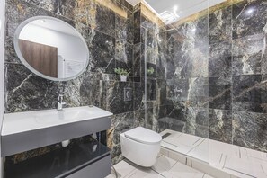 A modern bathroom with a marble wall, a round mirror, a white sink, and a toilet. - Magnifique Appartement a Constantine (Constantine)