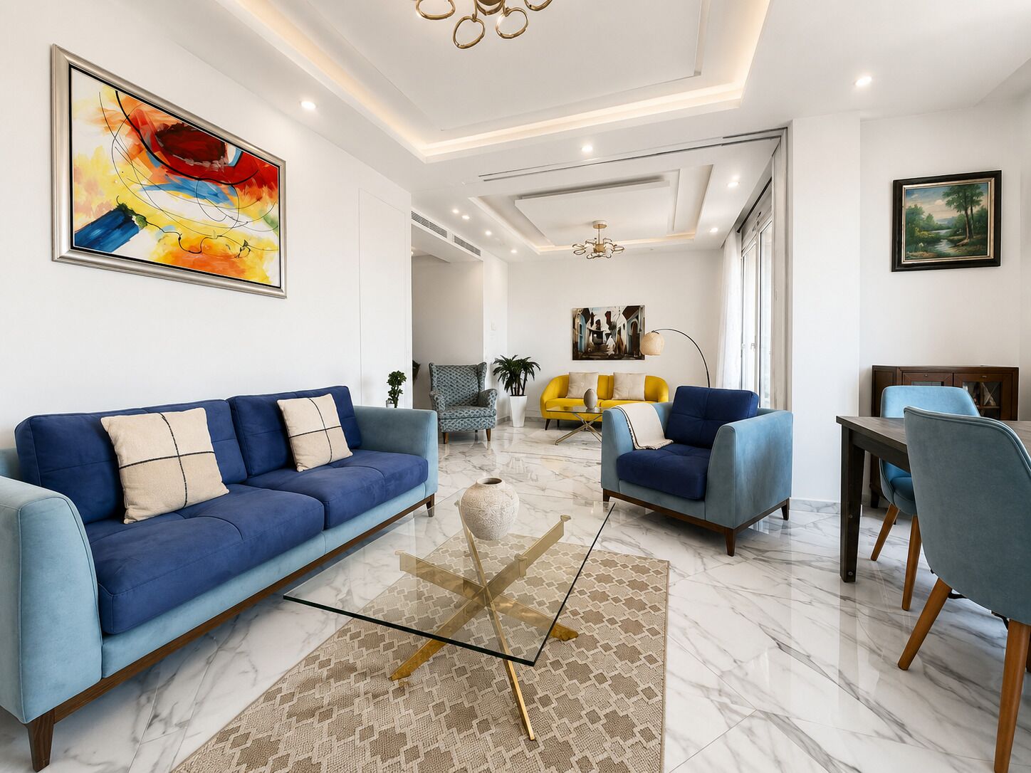 Un salon moderne avec un canapé bleu, un fauteuil jaune, une table à manger avec des chaises et un lustre.
