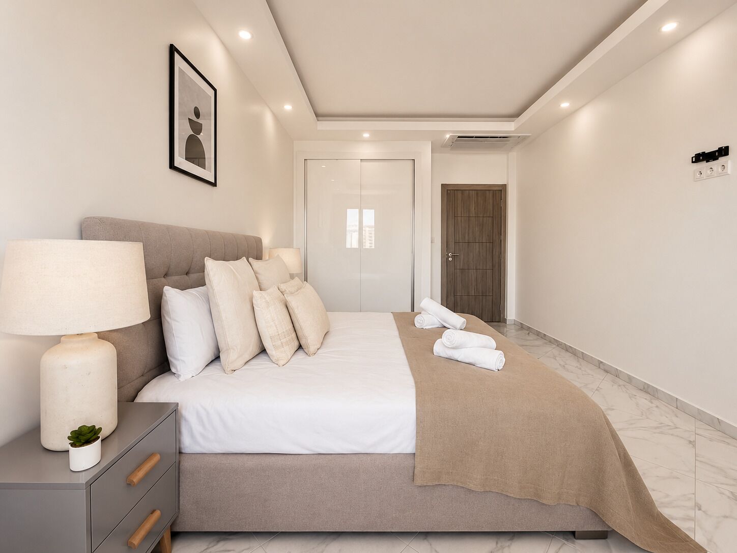 Una habitación de hotel moderna con una cama, lámpara de noche y vista al pasillo.