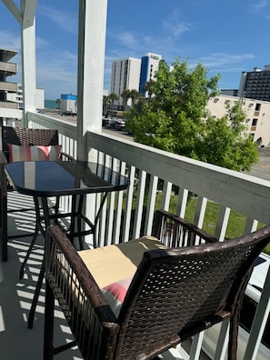 A balcony with wicker chairs and a table, overlooking a street with buildings and trees. - Whole Townhouse with Ocean View and only a 2-minute walk to the Beach! (Myrtle Beach)