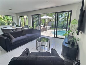 Ein modernes Wohnzimmer mit einer Couch, einem Couchtisch und Blick auf einen Pool und Garten.