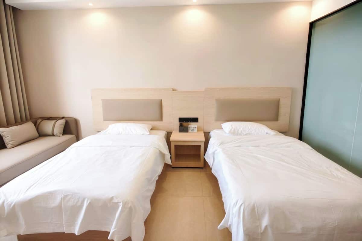 Ein Hotelzimmer mit zwei Betten, einem Schlafsofa, einem Nachttisch und einem großen Fenster.