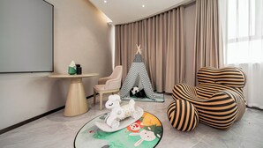 A modern living room with a flat-screen TV, a round table, a rocking horse, a striped bean bag, and a teepee with a panda. - Fu Hua Jun Yue Hotel (Luntai County)