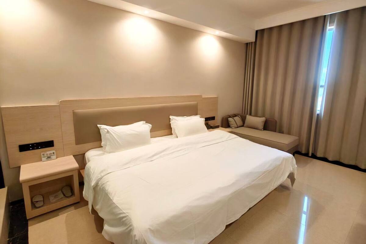 Ein Hotelzimmer mit einem großen Bett, Nachttischen, einer Sitzecke und einem Fenster mit Vorhängen.