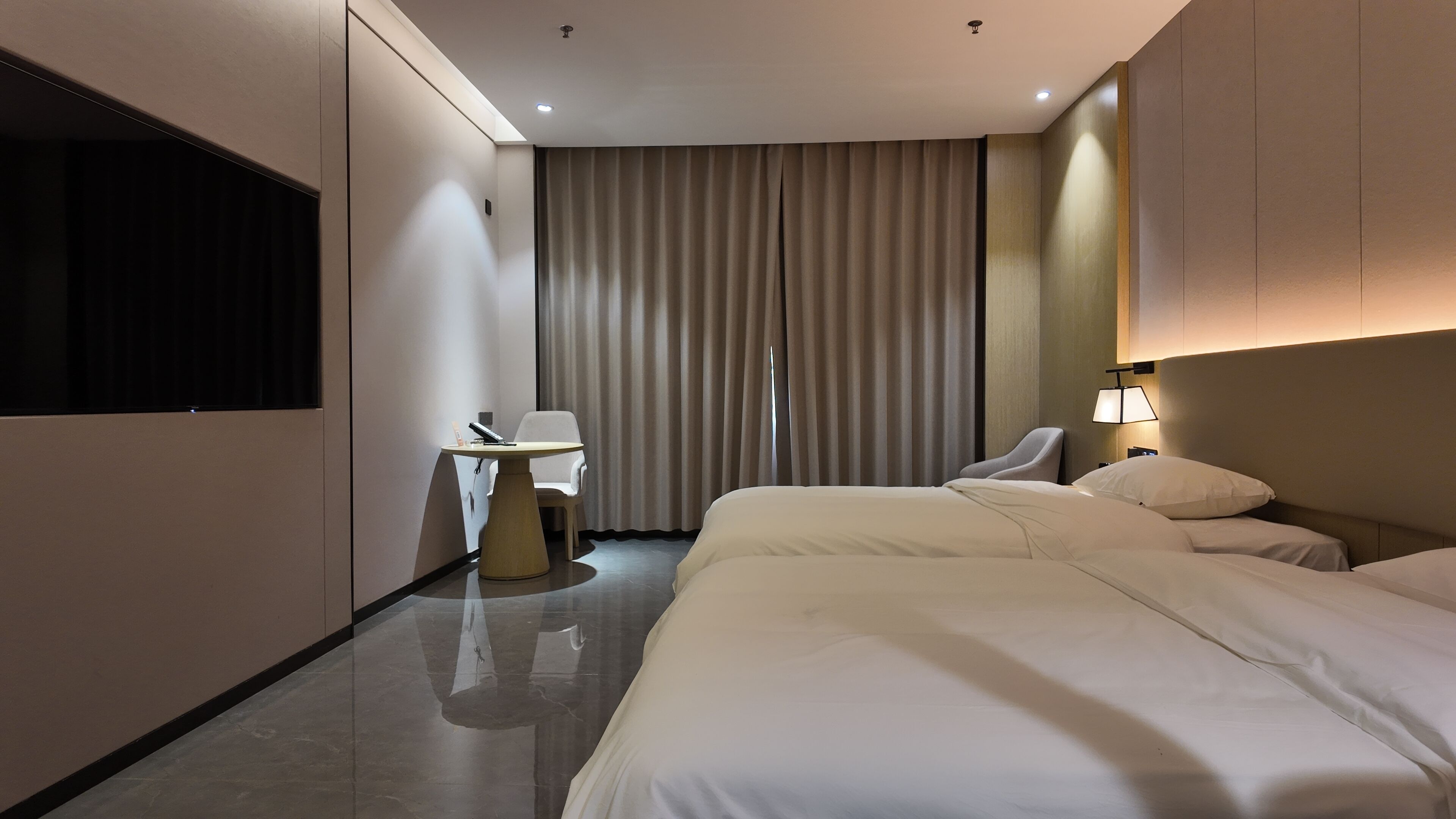 A hotel room with a bed, a desk, a chair, a lamp, and a large window with curtains.