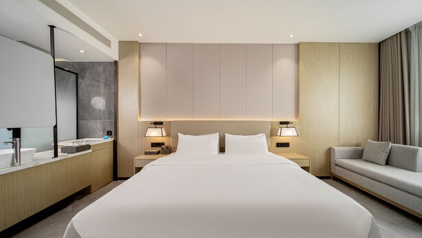 A modern hotel room with a large bed, bedside lamps, a sofa, a vanity with a mirror, and a large window with curtains. - Fu Hua Jun Yue Hotel (Luntai County)