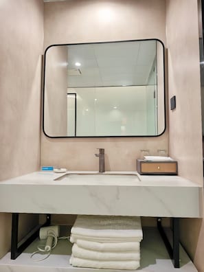 Un baño con lavabo de mármol, espejo, dispensador de toallas y cabina de ducha de vidrio.