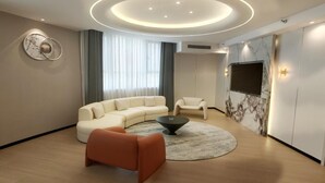 A modern living room with a sectional sofa, a coffee table, and a TV mounted on the wall. - Fu Hua Jun Yue Hotel (Luntai County)