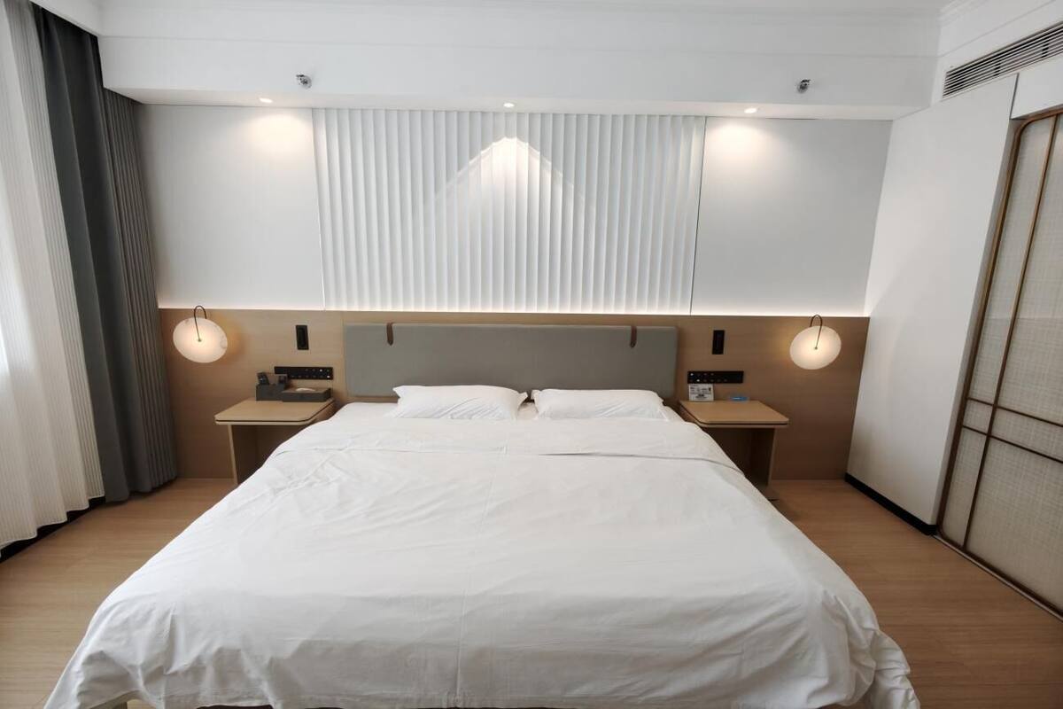 Ein Hotelzimmer mit einem großen Bett, Nachttischen, einem Kopfteil und einem Fenster mit Jalousien.