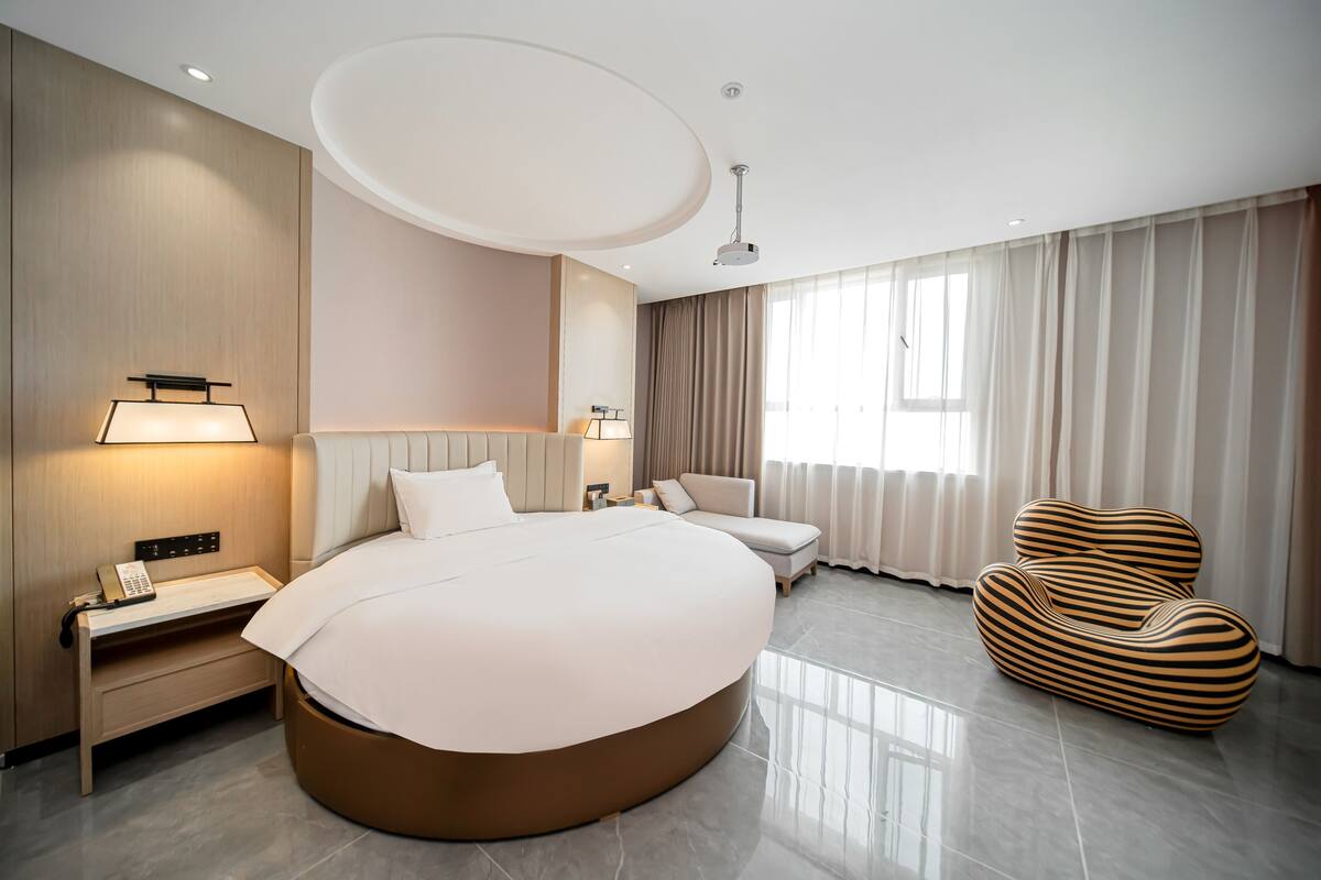 Ein modernes Hotelzimmer mit einem großen Bett, Nachttischen, einem Schreibtisch, einem Sessel und einem einzigartigen gestreiften Sofa.