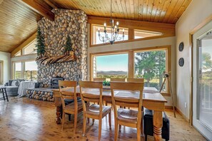 Une piĂšce spacieuse avec une cheminĂ©e en pierre, un plafond en bois et de grandes fenĂȘtres donnant sur lâextĂ©rieur.