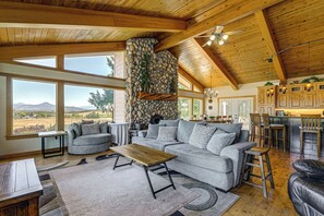 A spacious living area with a stone fireplace, large windows, and a kitchen with wooden cabinets. - Private Mtn-view Pool! Rogue River Valley Escape (Eagle Point)
