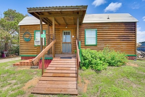 A wooden cabin with a porch, a staircase, and a small garden.