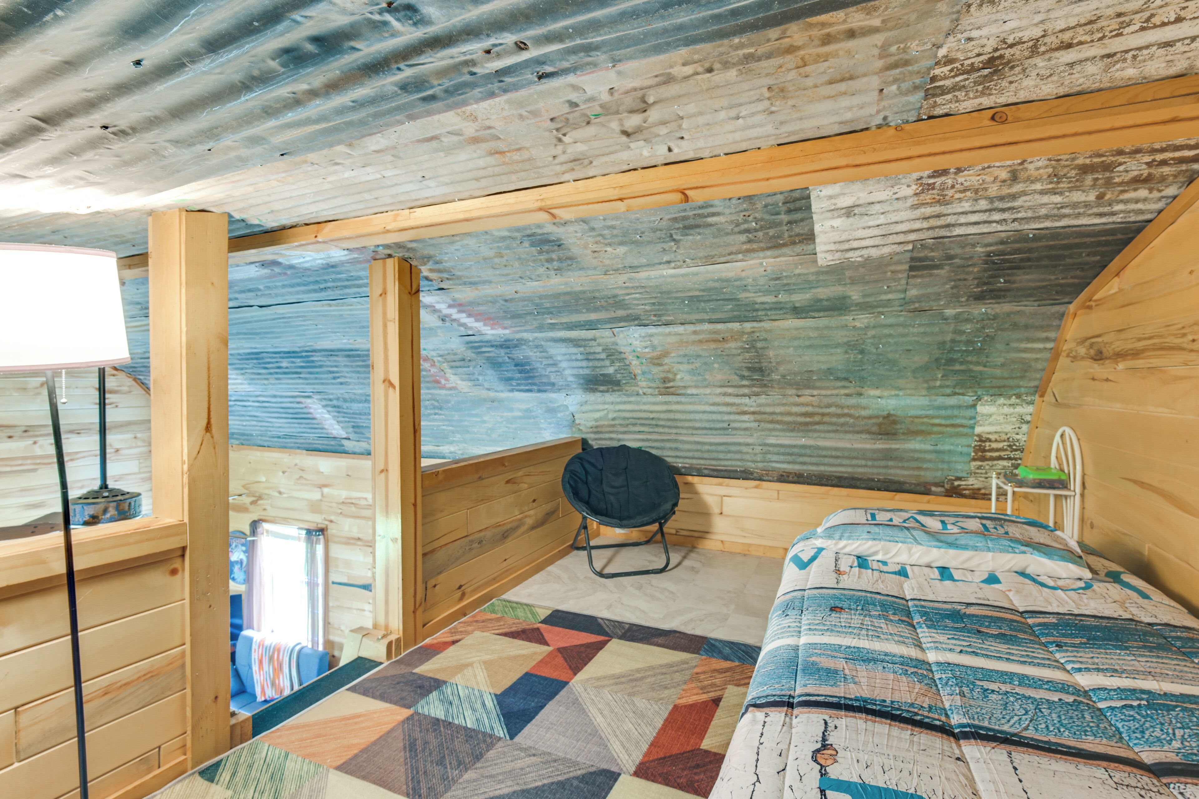 Una baita con interni in legno, un letto trapuntato, una sedia e una finestra.