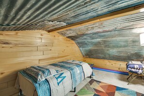 A room with a wooden bench, a patterned blanket, a colorful rug, and a corrugated metal ceiling.