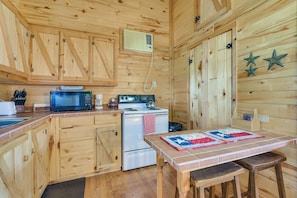 A wooden cabin kitchen with a microwave, stove, refrigerator, and a table with a quilt. - Cabin w/ Dock on Hubbard Creek Lake: Pets Welcome! (Breckenridge)