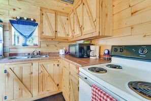 A wooden cabin kitchen with a stove, microwave, sink, and cabinets.
