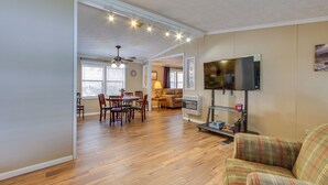 A living room with a television, a dining area with a table and chairs, and a kitchen area with a refrigerator.