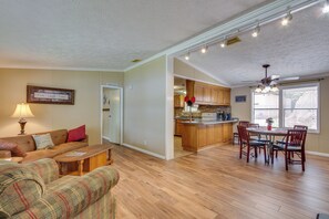 A living room with a sofa, a coffee table, and a dining area with chairs and a table. - Steps to Pickwick Lake! Home w/ Sunrooms & Views (Cherokee)