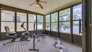 A covered outdoor gym area with exercise equipment, large windows, and a ceiling fan.