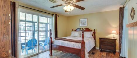 A bedroom with a wooden bed, a ceiling fan, a nightstand, and a view through a sliding glass door.