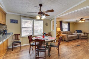A dining area with a round table, chairs, and a ceiling fan. There is a kitchen area with wooden cabinets and a countertop. - Steps to Pickwick Lake! Home w/ Sunrooms & Views (Cherokee)