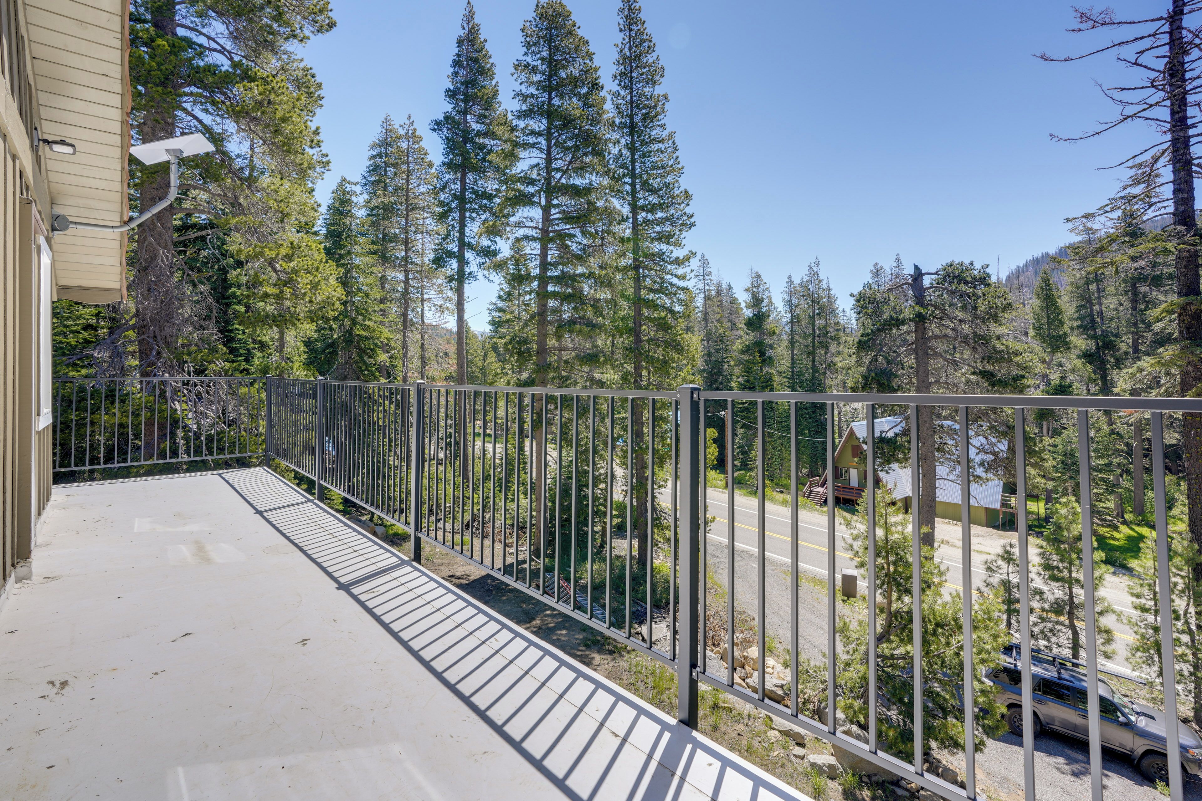 A balcony with a metal railing overlooking a road and forested area.
