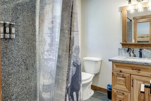 Ein Badezimmer mit Toilette, Holzschränken, einer Granit-Arbeitsplatte und einer Duschvorhang mit Hirschsilhouetten.