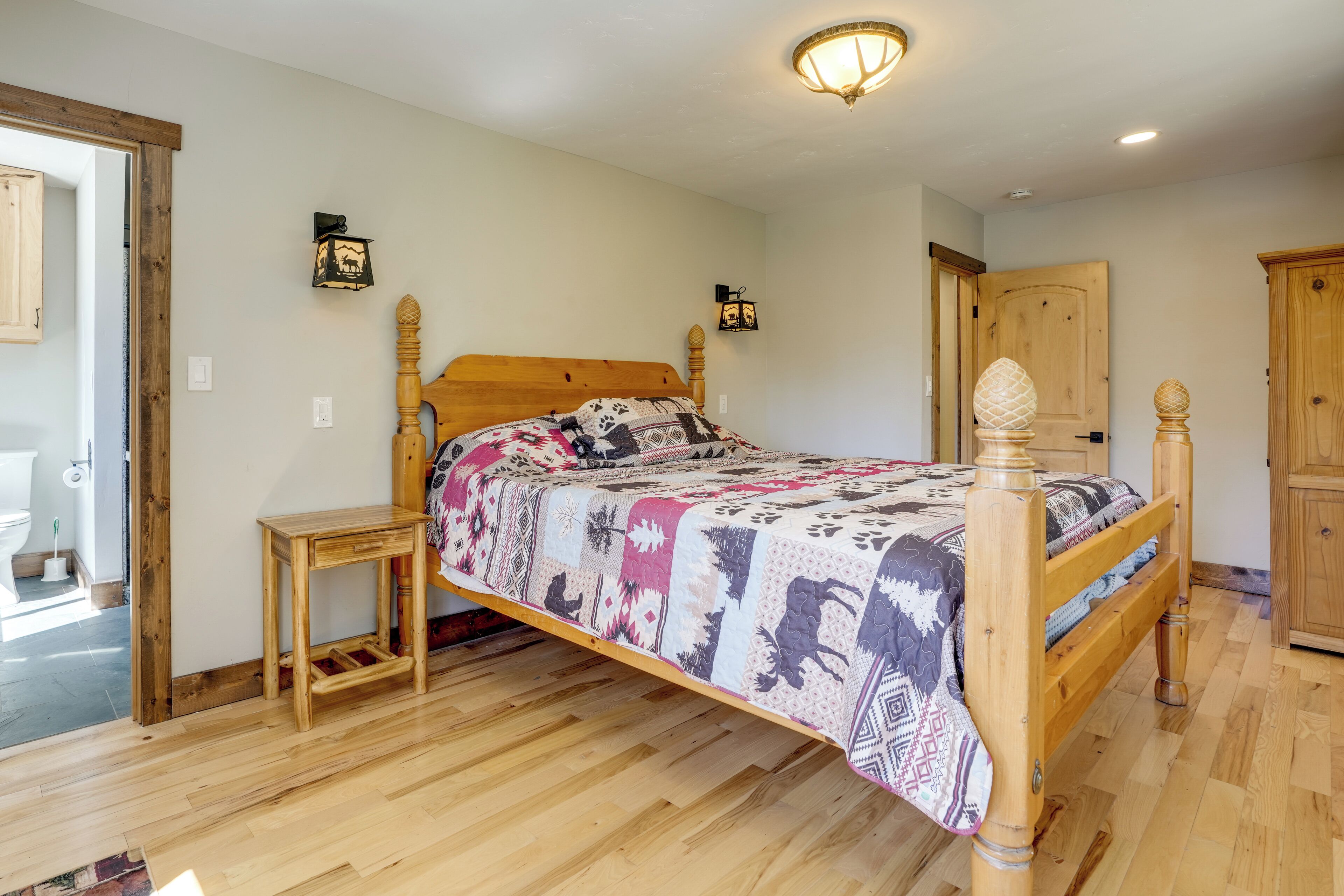 Un lit en bois avec une couvre-lit à motifs, une table de chevet et un luminaire fixé au mur.