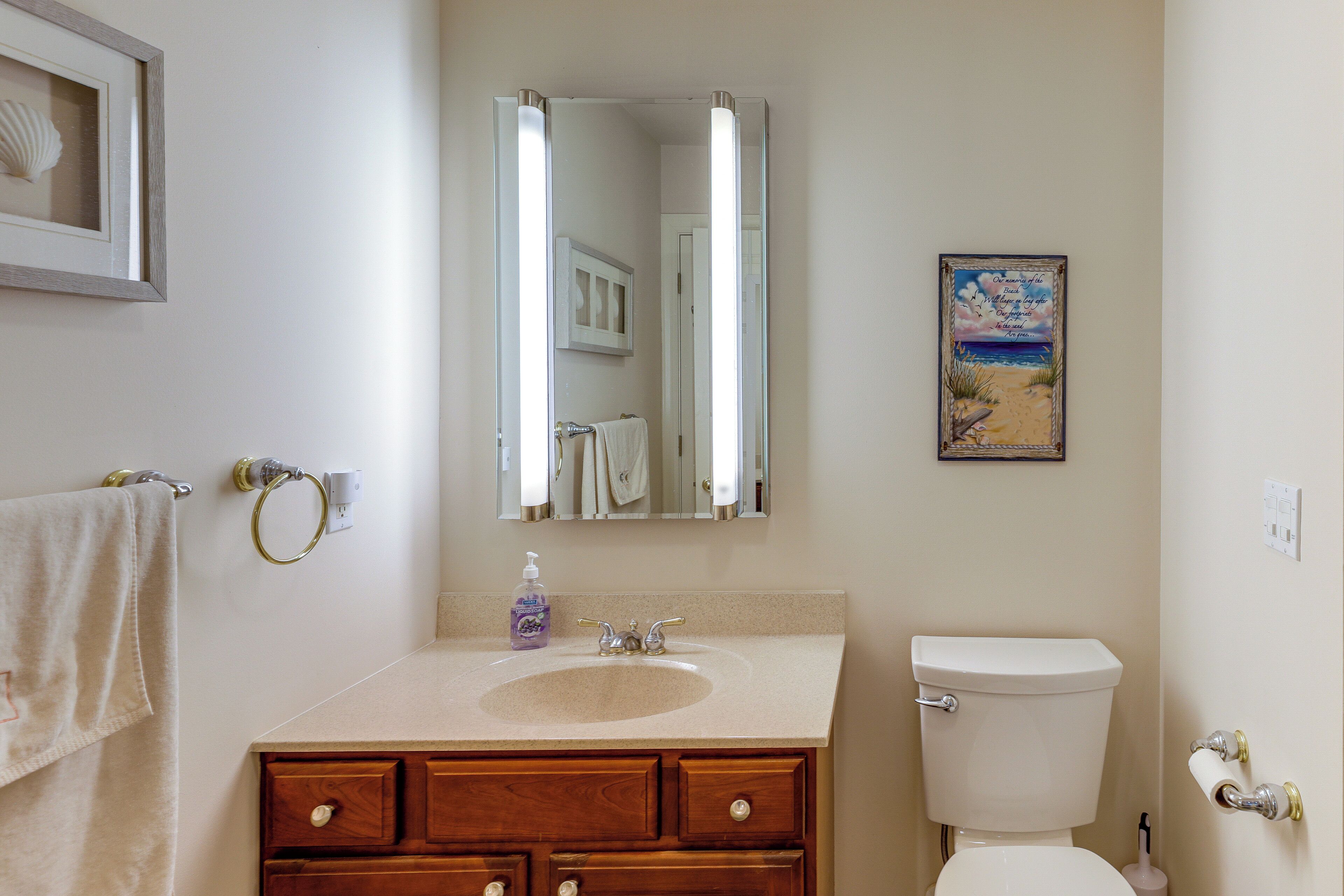 A bathroom with a sink, mirror, toilet, and a framed picture on the wall.