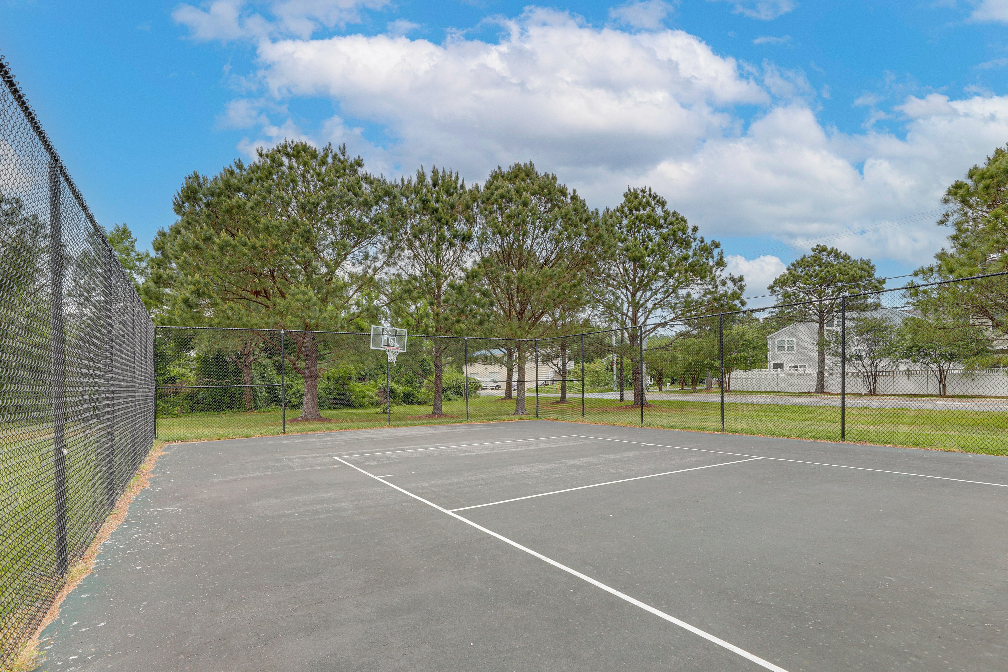 En udendørs basketballbane med hegn, træer og en blå himmel.