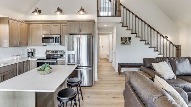 A modern kitchen with stainless steel appliances, a central island, and a staircase leading to an upper level. - Boat & Fish on Cow Creek! Brand-new Pierre Home (Pierre)