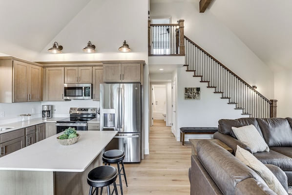 A modern kitchen with stainless steel appliances, a central island, and a staircase leading to an upper level.
