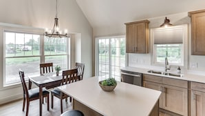 A kitchen with a large island, wooden cabinets, and a view of the outdoors. - Boat & Fish on Cow Creek! Brand-new Pierre Home (Pierre)