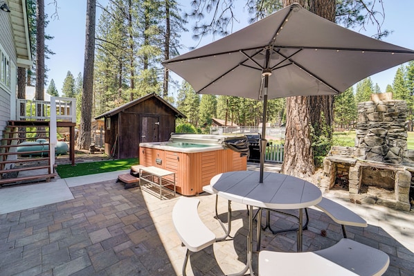 A patio with a table and benches, a hot tub, and a stone fireplace.