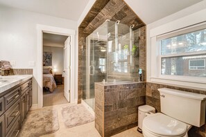 A bathroom with a glass shower enclosure, a toilet, a sink, and a window.