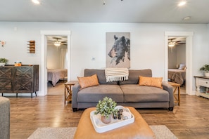 A living room with a grey sofa, a wooden coffee table with a plant, and a painting on the wall.