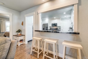 A modern kitchen with white cabinets, a stainless steel refrigerator, and a black countertop. There are two white stools and a small table with a plant. - Outdoor Adventure Base w/ Private Patio in Calpine (Calpine)