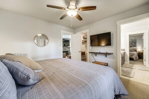 Un dormitorio con cama, ventilador de techo, televisor montado y vestidor.