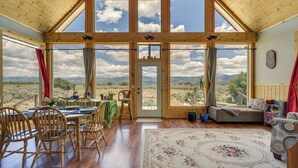 Ein geräumiger Raum mit hohen Decken, großen Fenstern, einer Essecke mit Holzsesseln, einem Sofa und einem Teppich mit Blumenmuster.