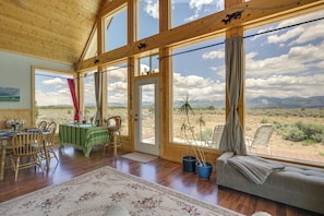 A spacious room with wooden walls and large windows, a dining area with a table and chairs, and a sofa with a view of the desert landscape.