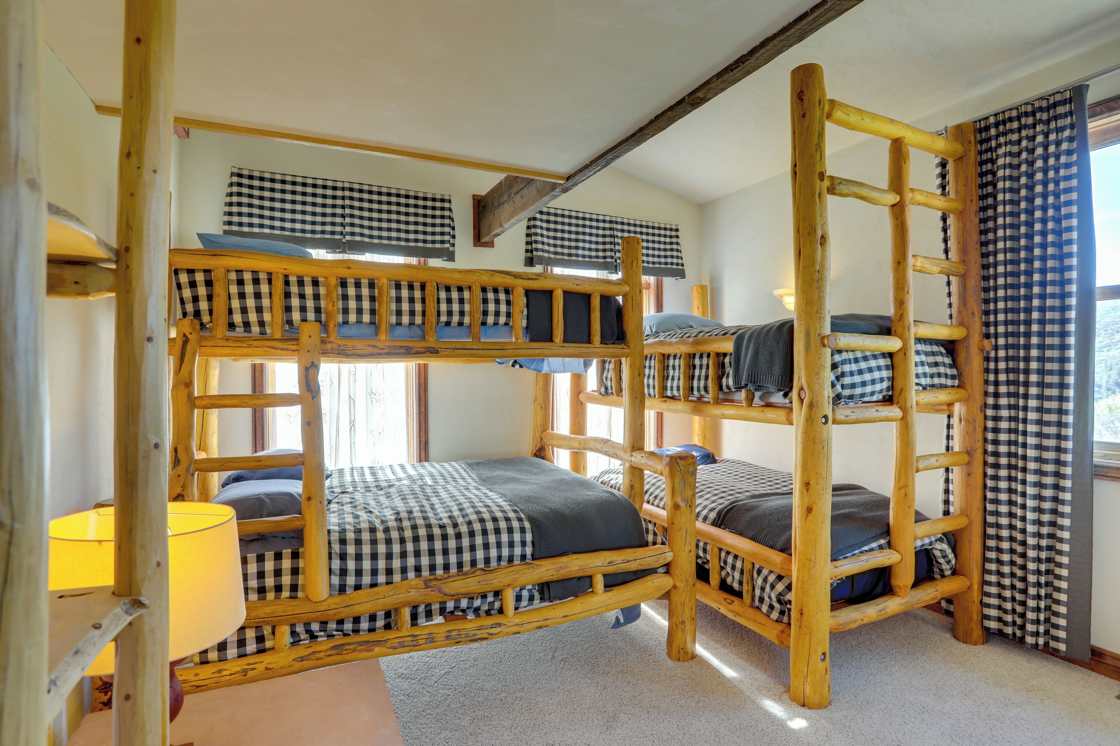 A bunk bed room with a wooden ladder, checkered bedding, and a lamp.