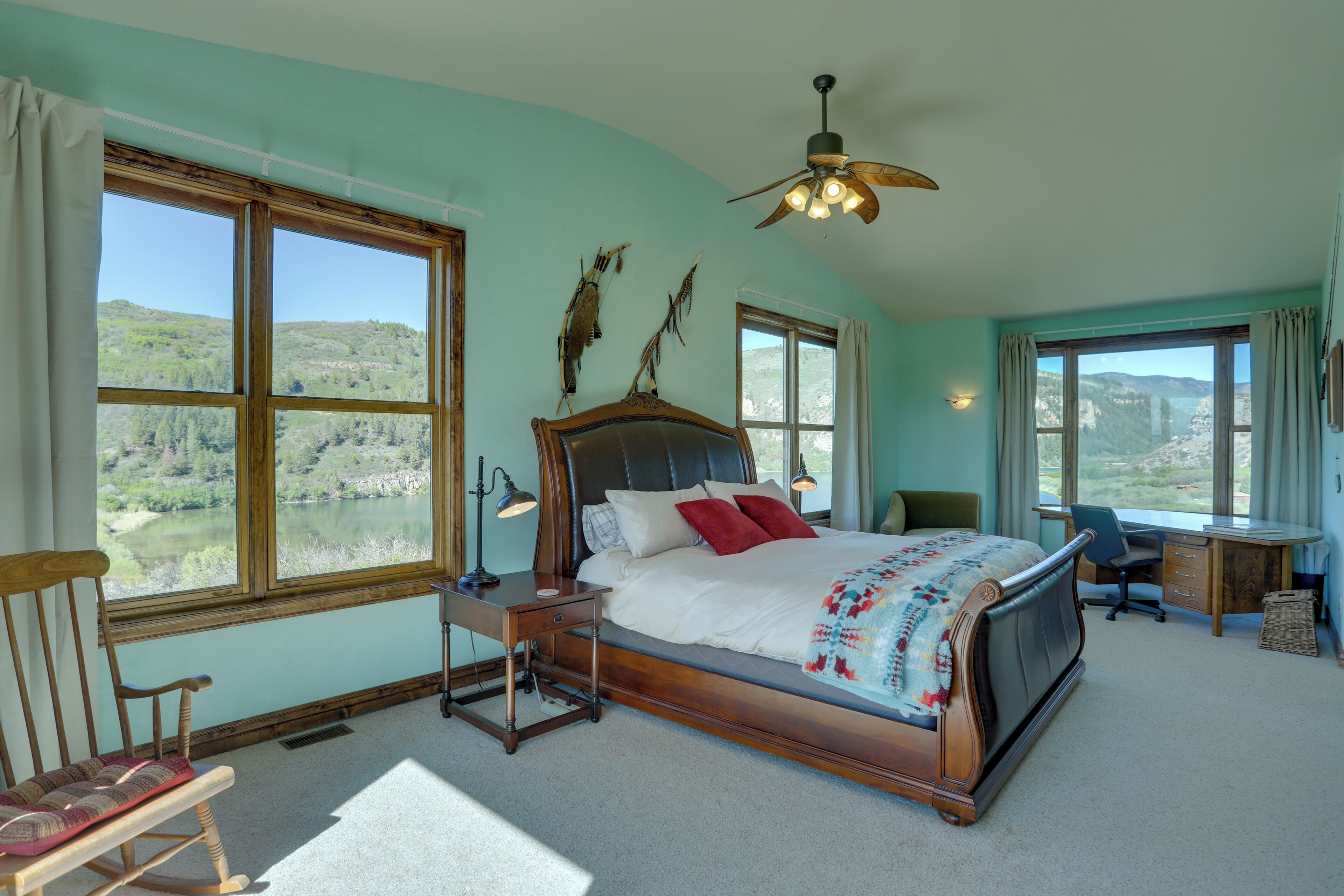 A bedroom with a large bed, a desk, a chair, and a view of a lake.