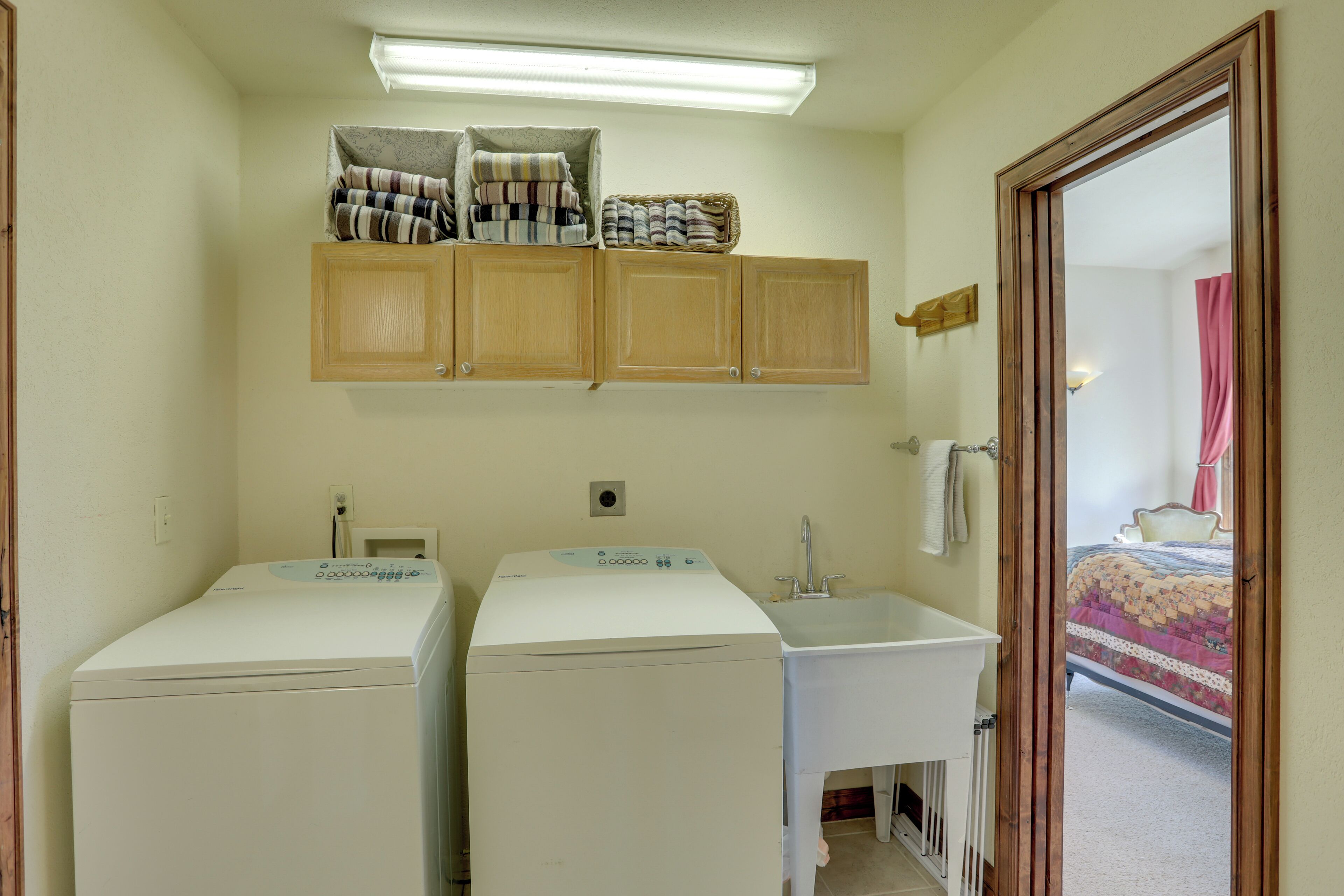 A laundry room with two washing machines, a sink, and wooden cabinets above.