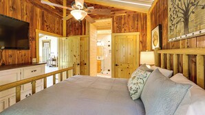 A wooden cabin-style bedroom with a bed, pillows, a ceiling fan, a TV, and a door leading to a bathroom. - Fish On-site! 35-acre Escape Near Cedar Creek Lake (Malakoff)